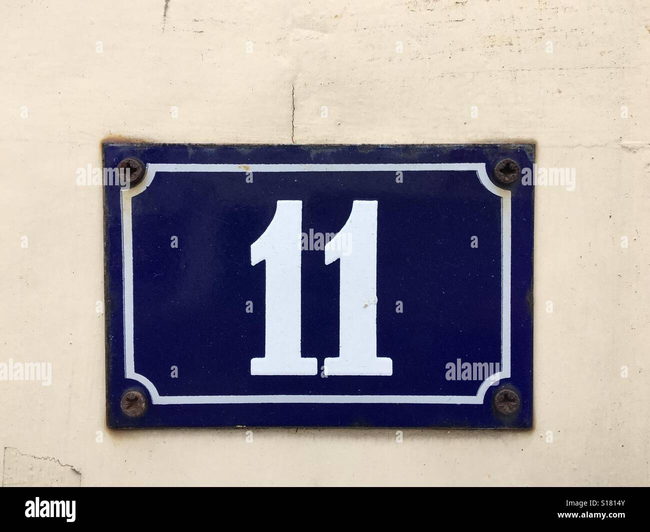 Dunkel blaue Nummer Metallplakette mit Nummer 11 in weiß auf einer bemalten Wand angebracht Stockfoto