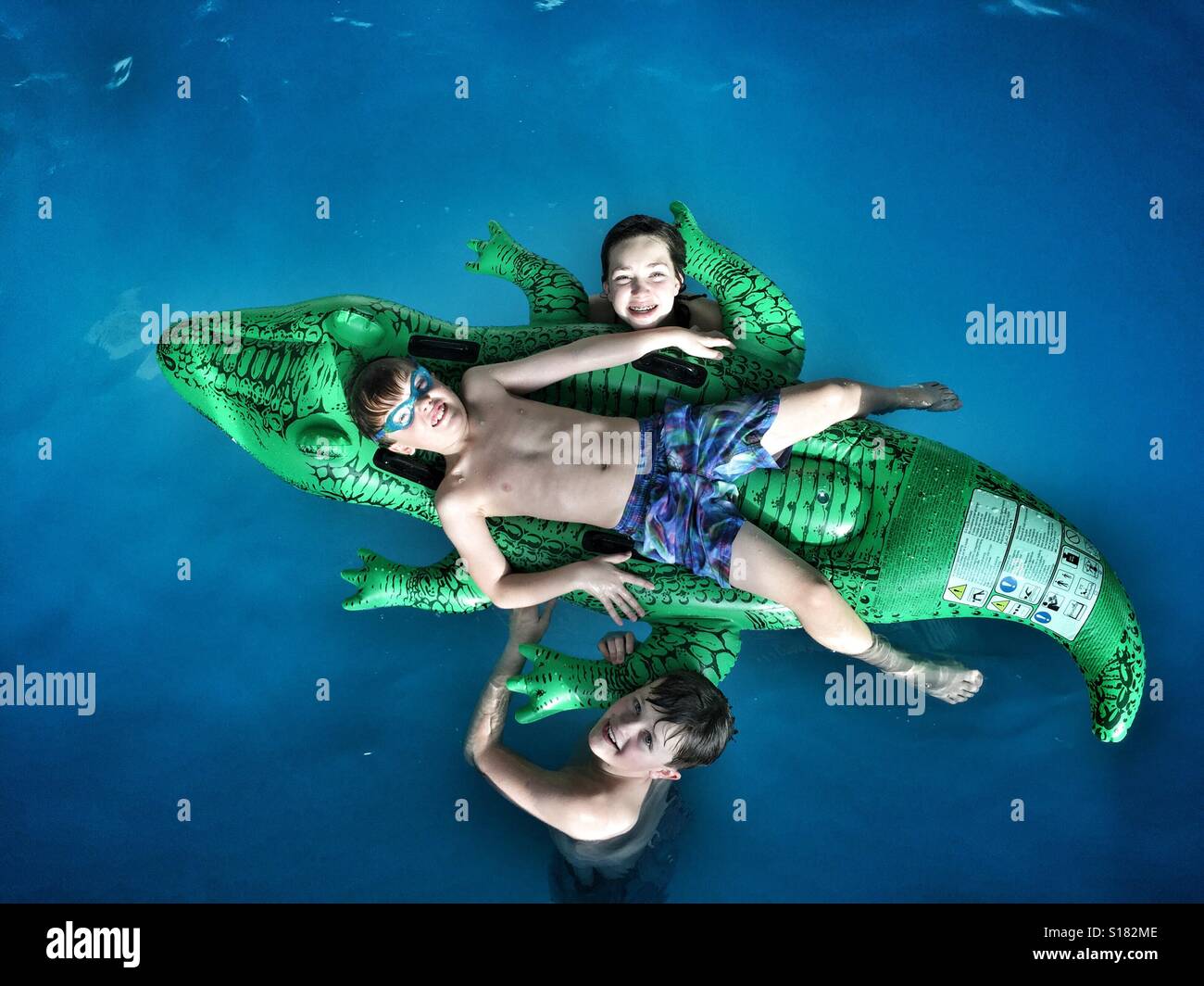 Kinder stellen für ein Familienfoto, da sie in einem Schwimmbad mit ein aufblasbares Bett in der Form eines Krokodils zu spielen. Stockfoto