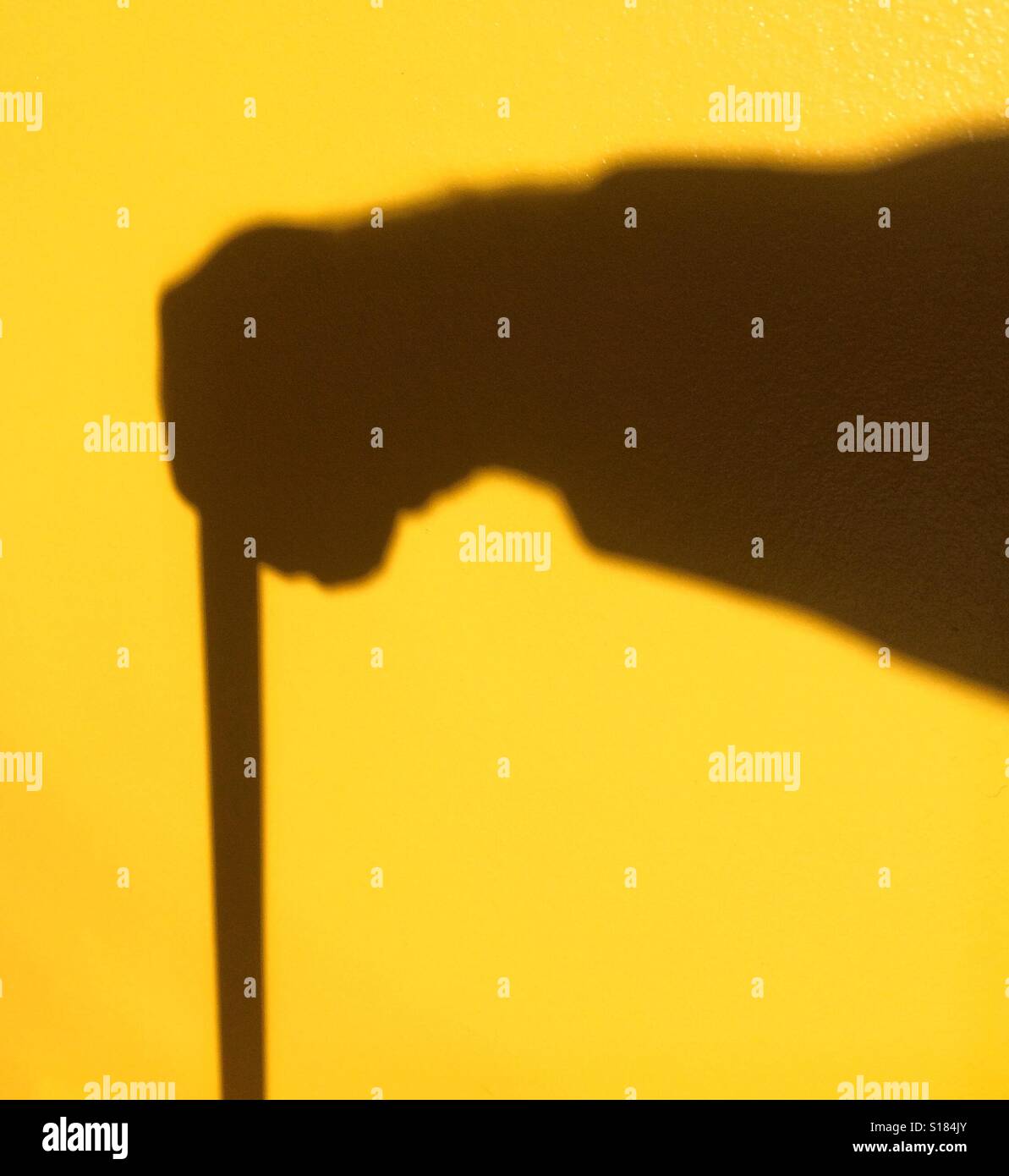 Der Schatten eines Mannes mit einem Gehstock auf gelbem Hintergrund Stockfoto