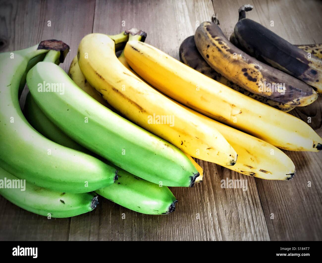 Bananen in den verschiedenen Phasen der Reifung auf eine Holzoberfläche. Stockfoto