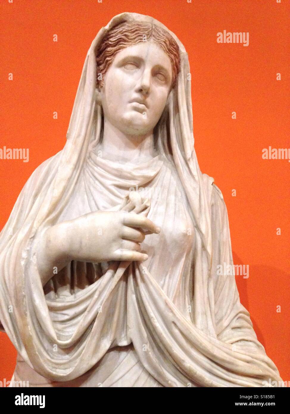 Klassische Marmorstatue eines römischen Mädchens mit orangem Hintergrund. Stockfoto