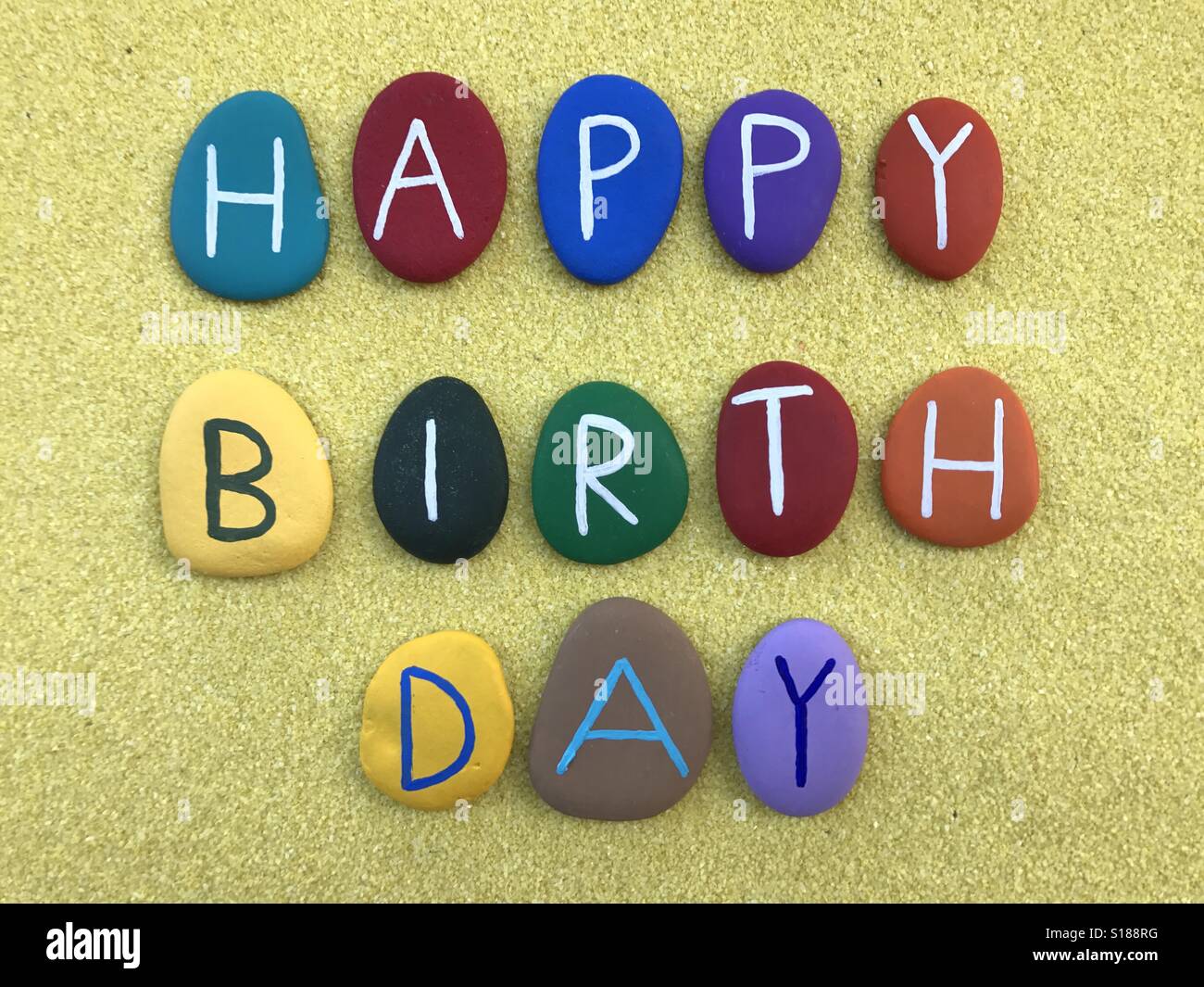 Happy Birthday mit farbigen Steinen Buchstaben über gelben sand Stockfoto