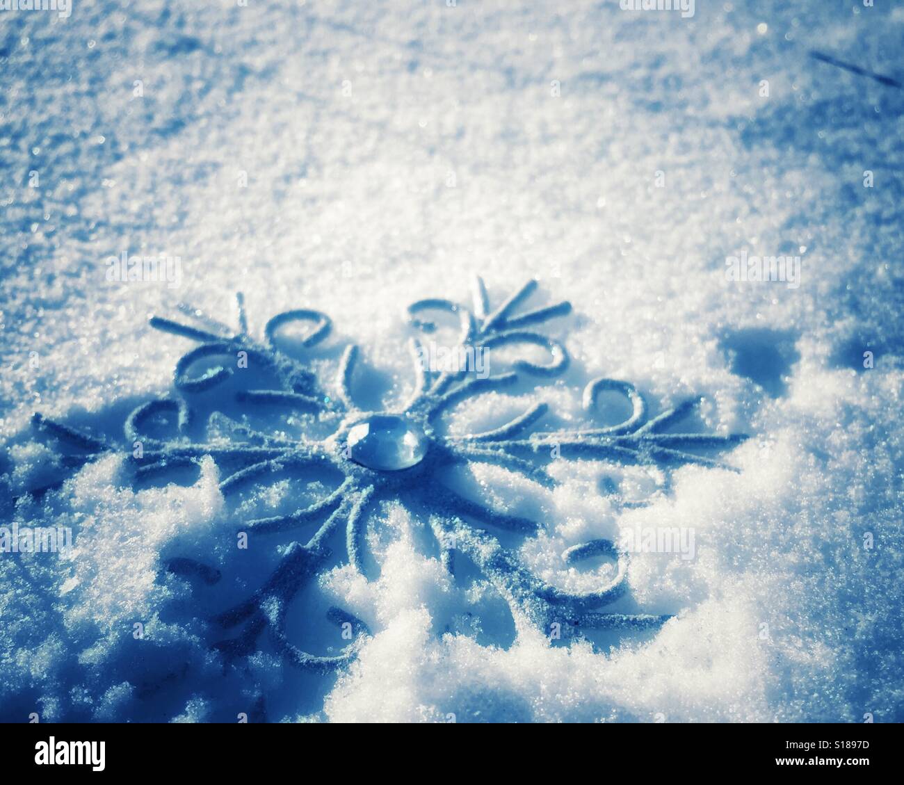 Schneeflocke geformt Ornament im Schnee liegen. Kühle Töne. Raum für Kopie. - Smartphone-aufgenommenes Stockfoto