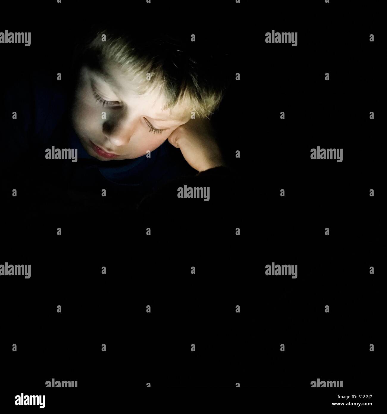 Ein Junge liest auf einem digitalen Gerät in der Nacht. Stockfoto