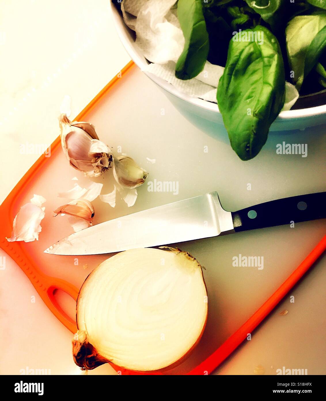 Schneidebrett mit Zwiebel-Knoblauch-Basilikum und ein Messer - Smartphone-aufgenommenes Stockfoto