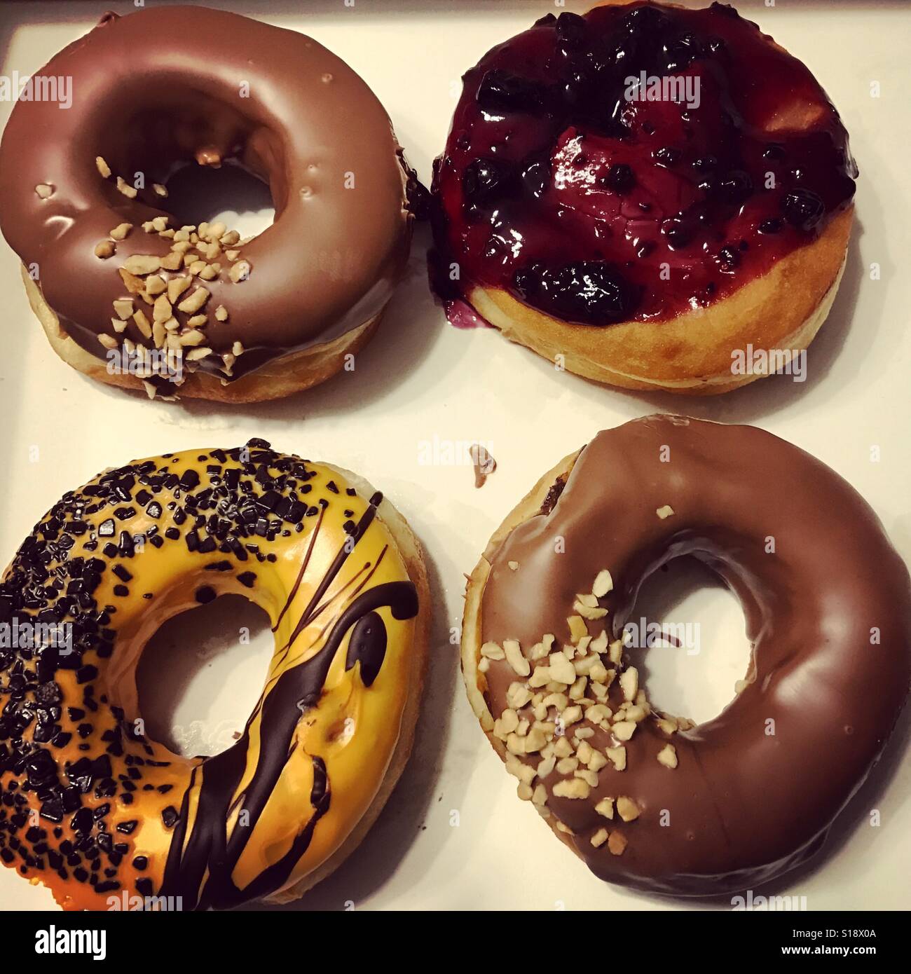 Leckere Donuts. Süßen Leckereien. Bunt und lecker Donuts in einer Box. Schokolade und Erdnüssen, Beeren und Sahne und Schokolade und orange Donuts. Donuts für Wüste. Wüste Stockfoto