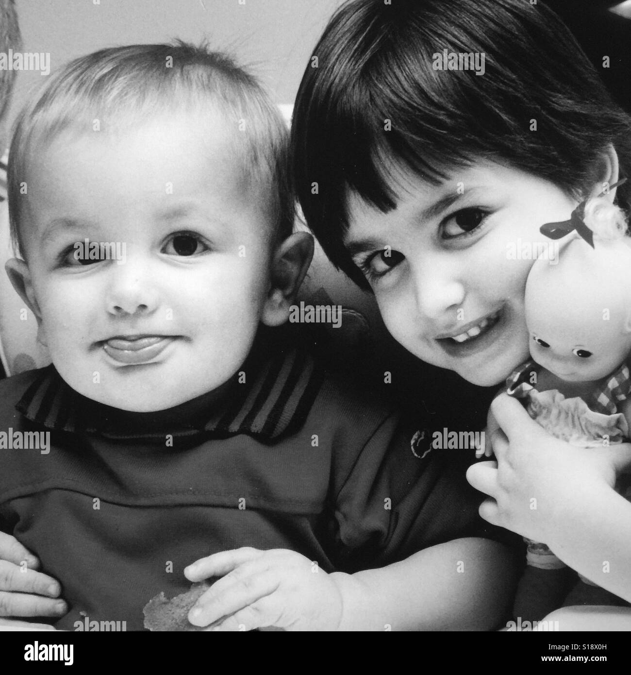 Ein schwarz-weiß Bild von einem Kleinkind Jungen und seine Schwester, die eine Babypuppe hält Stockfoto