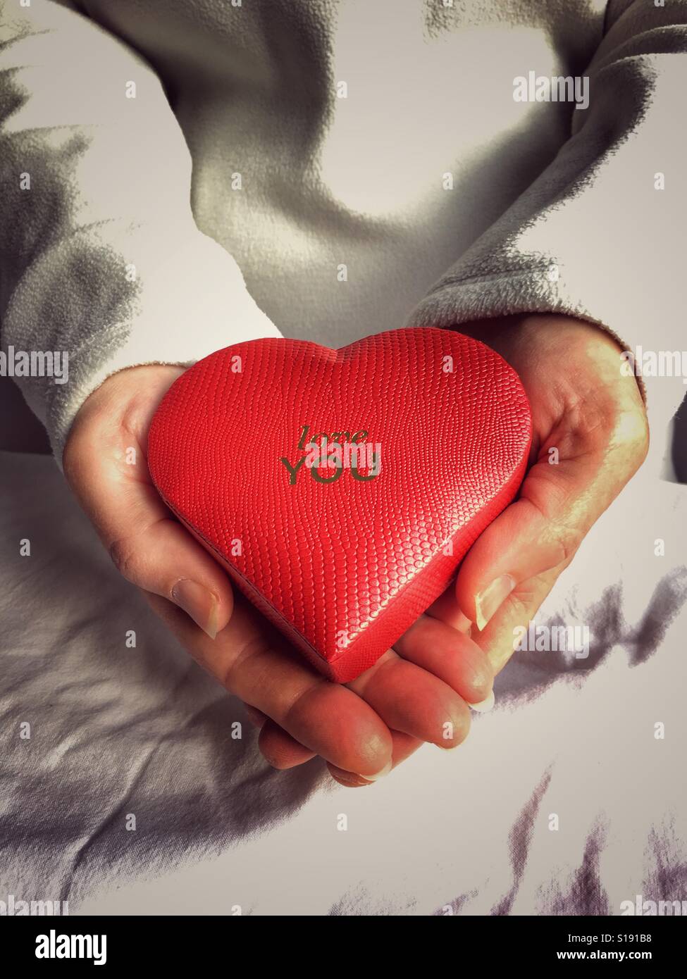 Rote herzförmige Box mit Botschaft, liebe dich, in Händen - Smartphone-aufgenommenes Stockfoto