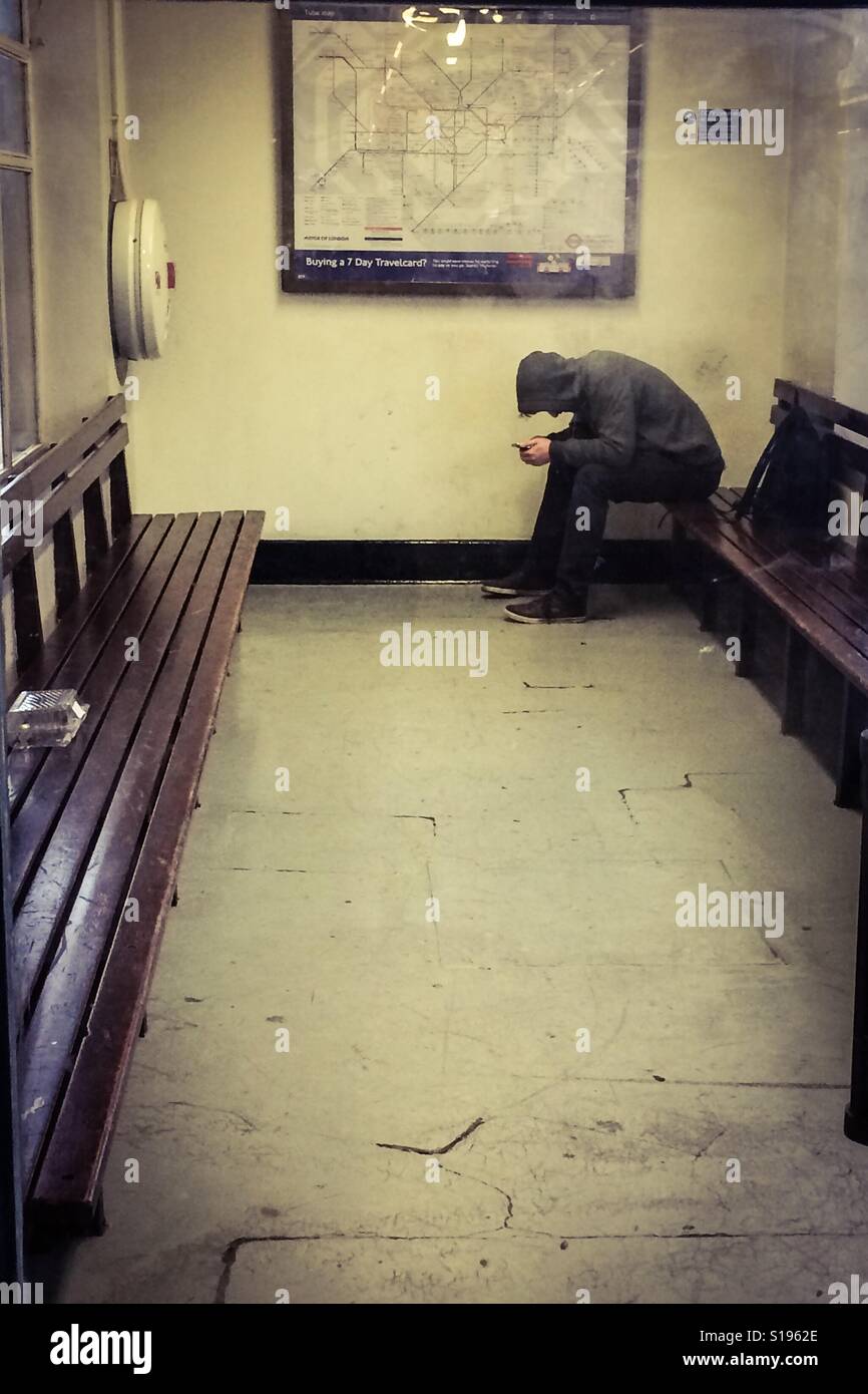 Junger Mann kauerte über Telefon - Smartphone-aufgenommenes Stockfoto