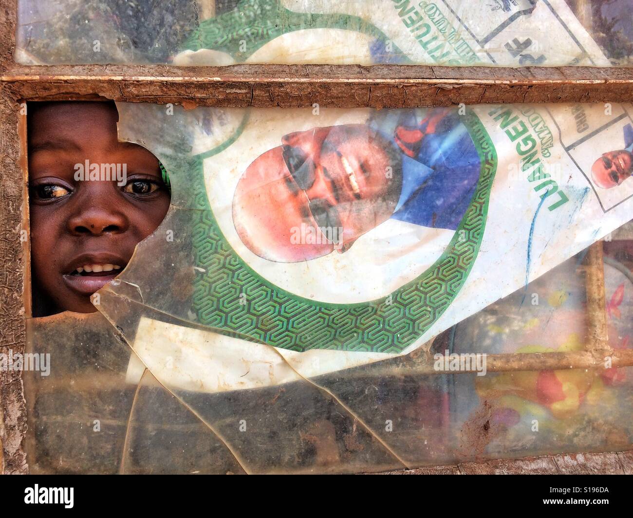 Ein junges Mädchen schaut durch die zerbrochenen Fenster ihrer Schulklasse in Chipata, Sambia. Stockfoto