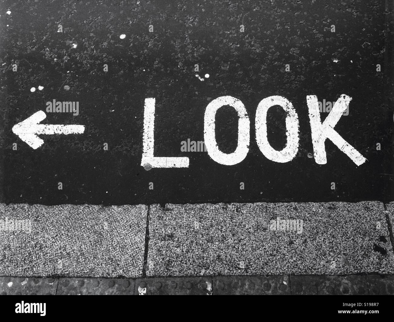 Suchen Sie linken Zeichen. Das Wort "Look" auf der Straße in fetten weißen Großbuchstaben, mit Pfeil nach links gemalt. Stockfoto