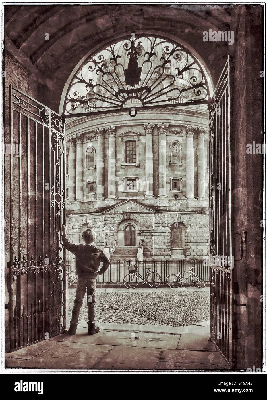 Ein 7 Jahre alter Junge steht in einem reich verzierten Torbogen & blickt auf das Radcliffe Kamera Bibliotheksgebäude im Bereich Universität von Oxford, England, UK. Was ist dieser junge denken? Foto © COLIN HOSKINS. - Smartphone-aufgenommenes Stockfoto