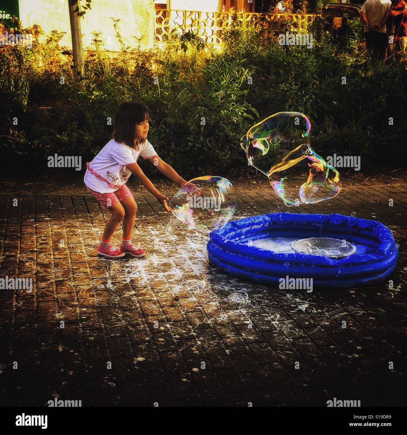Junges Mädchen mit einer Seifenblase in einen kleinen Pool auf der Straße spielen Stockfoto