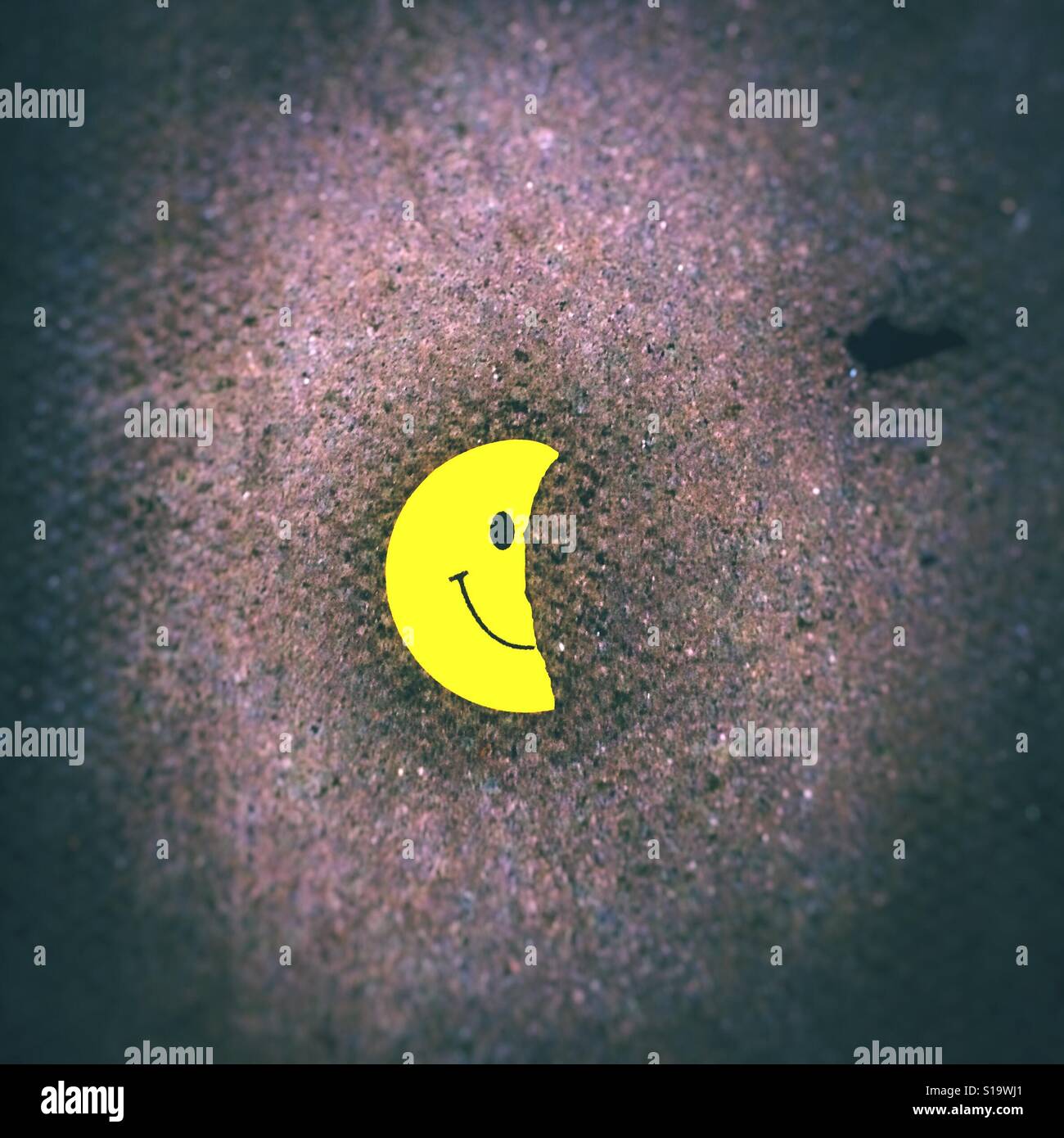 Halb einen Smiley Emoji Aufkleber auf einer Pflasterung Stockfoto