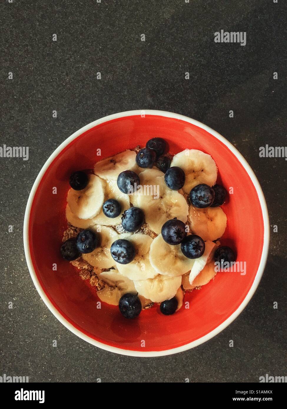 Gesundes Frühstück. Schüssel Müsli mit frischen Bananen und Heidelbeeren garniert. Kopieren Sie Raum. - Smartphone-aufgenommenes Stockfoto
