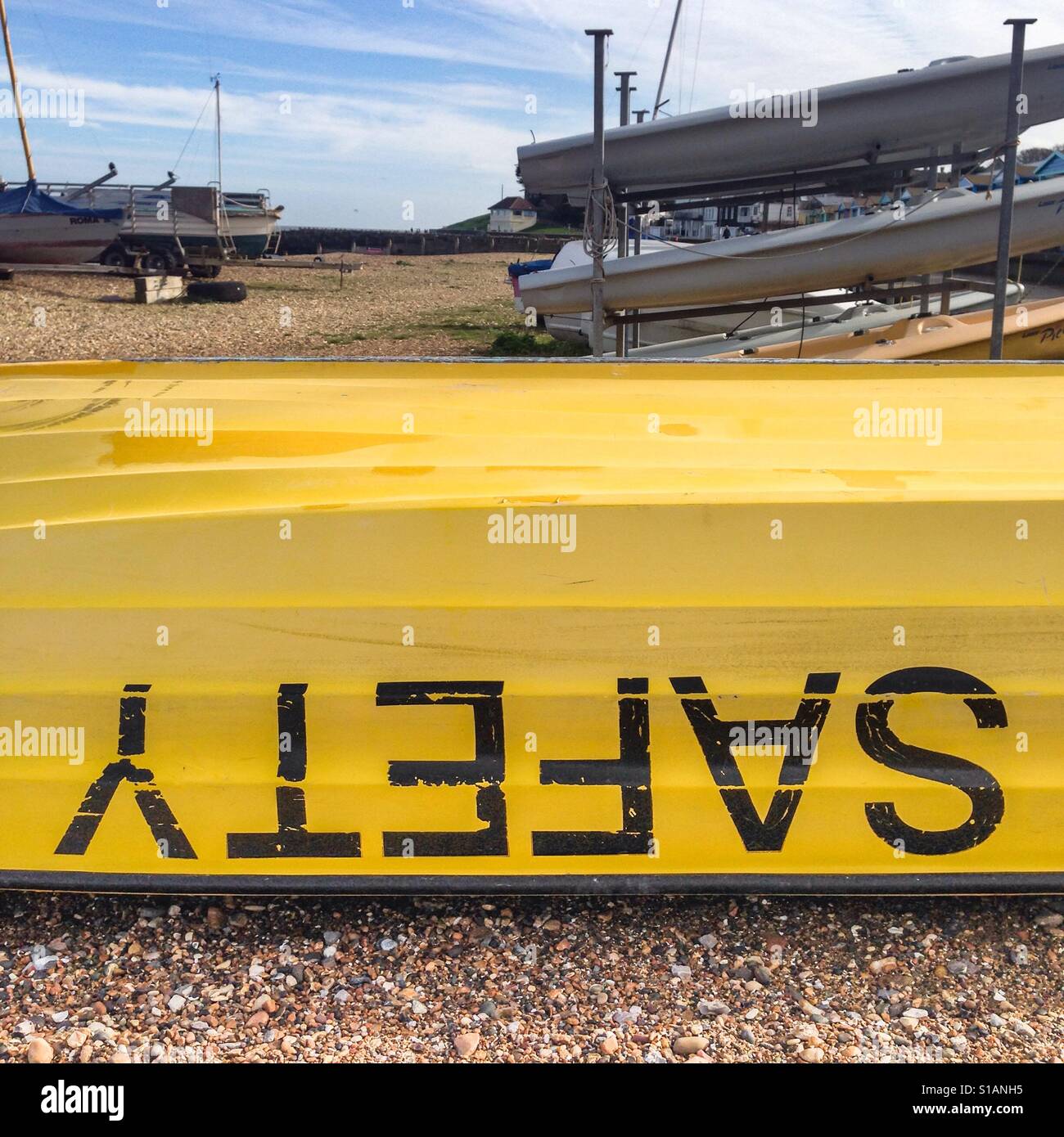 Sicherheit geschrieben auf dem Kopf stehend auf einem gelben Boot, Rettungsboot auf einem Kiesstrand Stockfoto