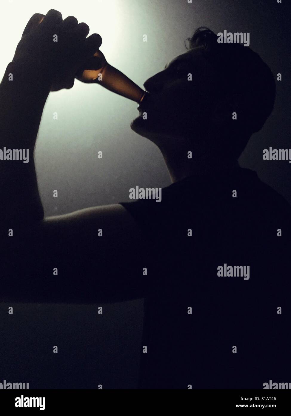 Silhouette eines jungen Mannes aus einer Glasflasche trinken. - Smartphone-aufgenommenes Stockfoto