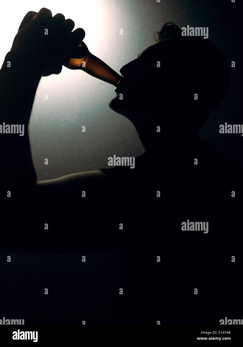 Silhouette eines jungen Mannes aus einem Glas Bierflasche trinken. - Smartphone-aufgenommenes Stockfoto