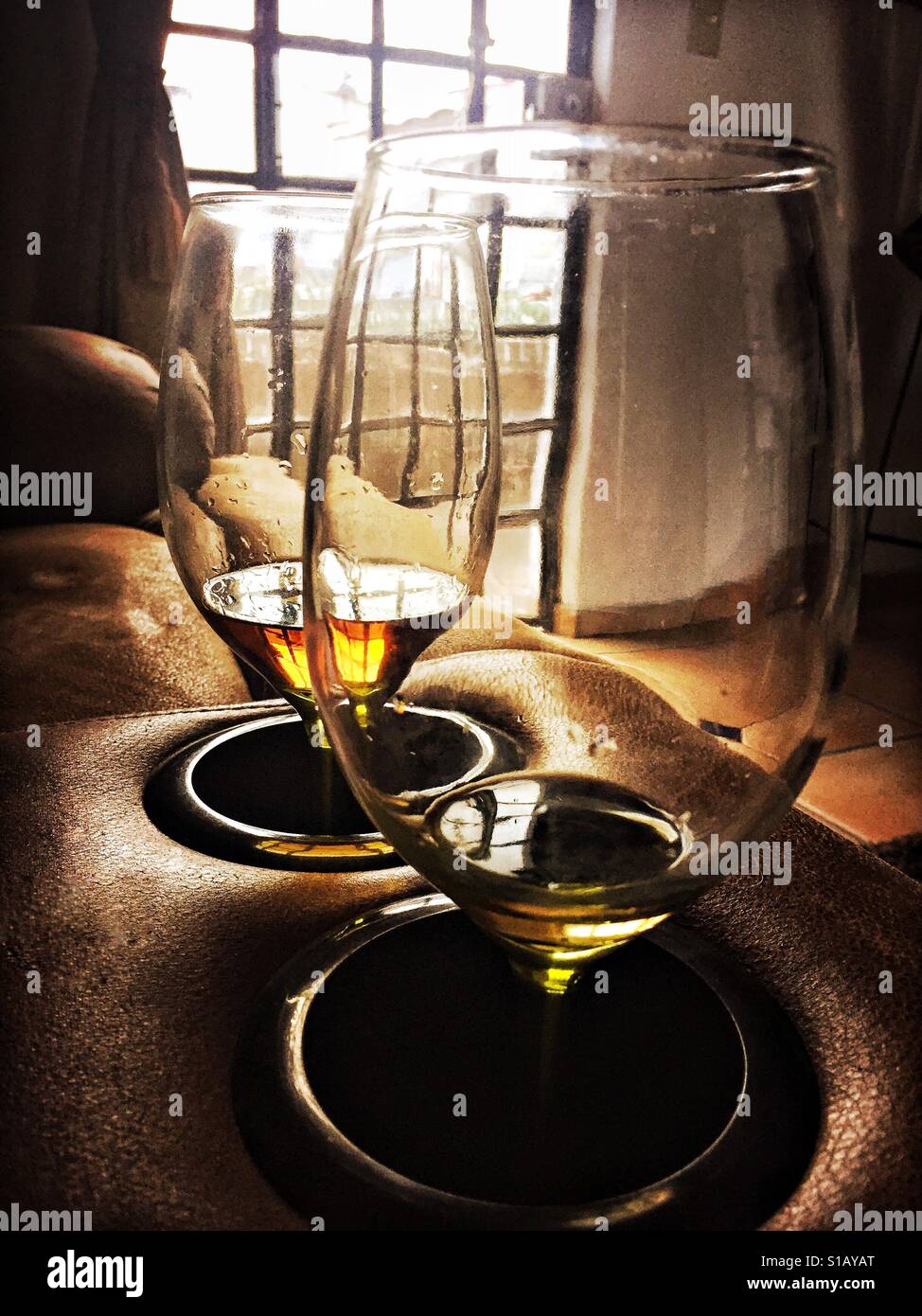 Zwei Gläser halten nippen Tequila in den Getränkehalter Bequemsessel durch Fenster am Abend beleuchtet. Stockfoto