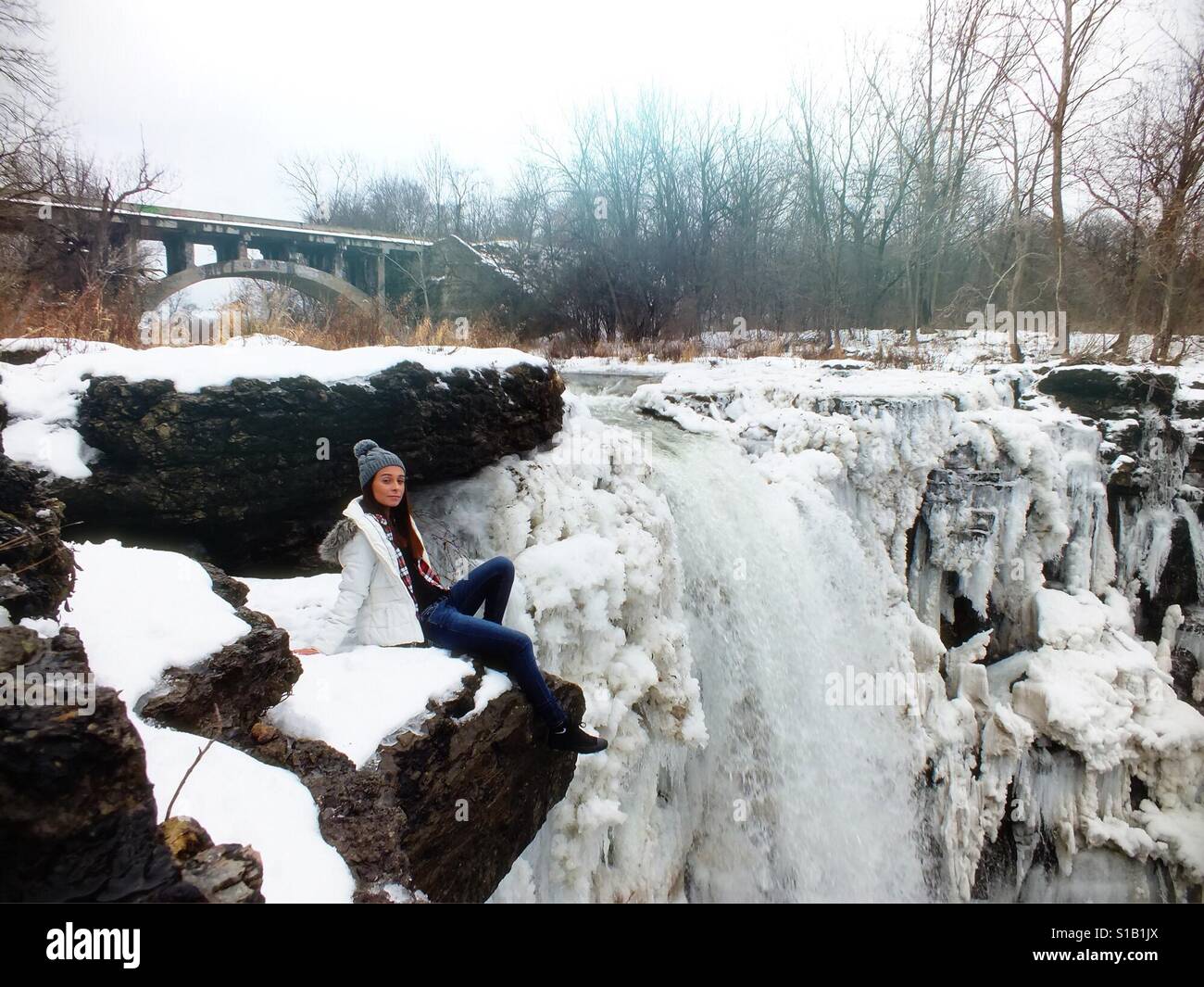 Mädchen sitzen durch die verschneiten Wasserfälle Stockfoto
