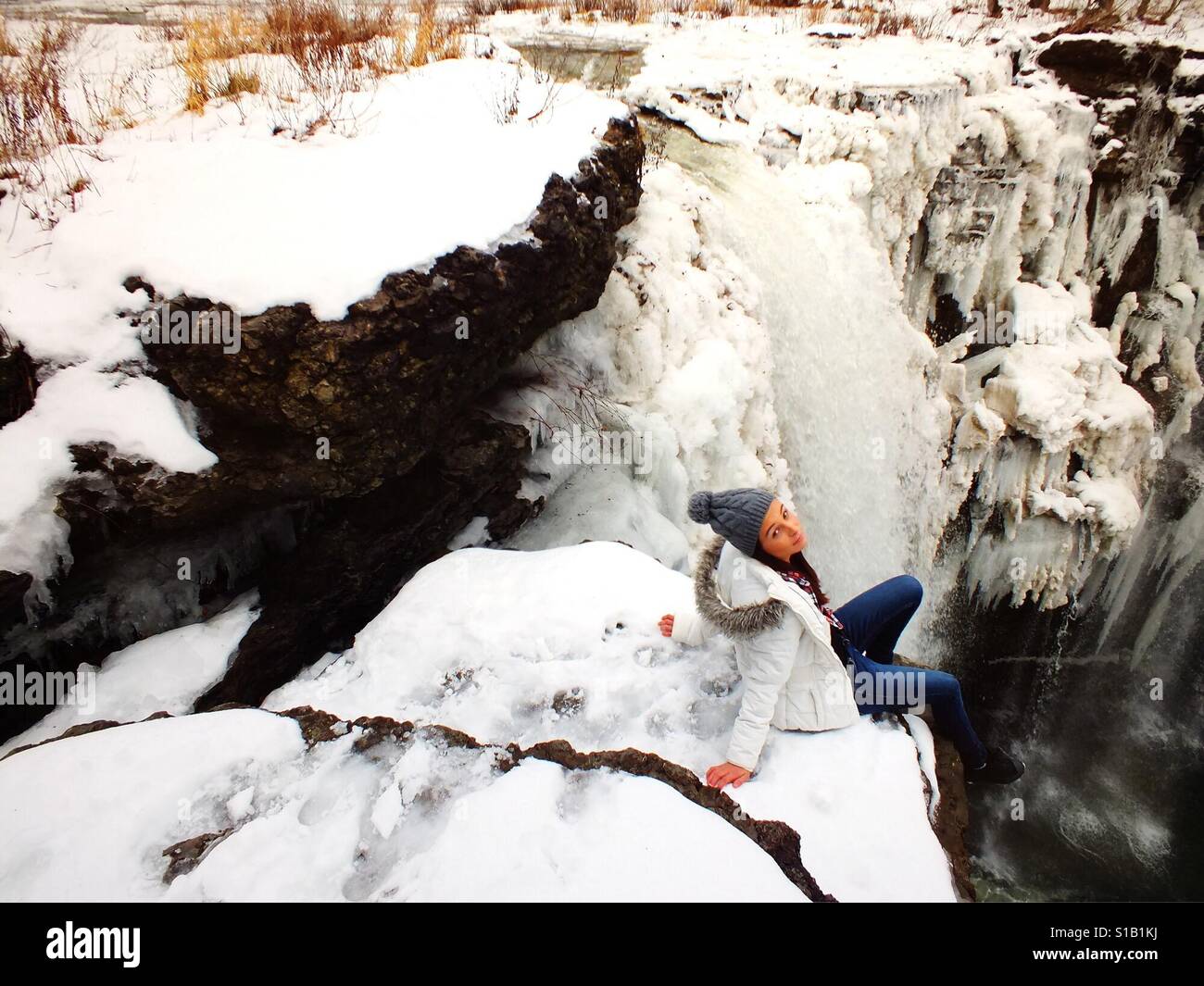 Mädchen sitzen von verschneiten Wasserfall Stockfoto