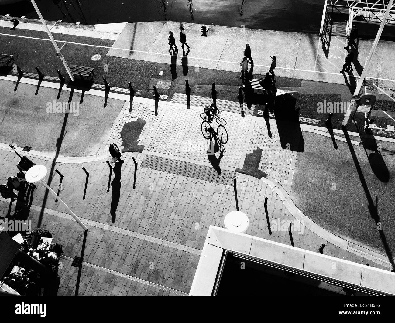 Schwarz / weiß Foto der frühen Morgensonne lange Schatten werfen, als ein Radfahrer fährt mit Poole Quay, Dorset, England, UK. Stockfoto