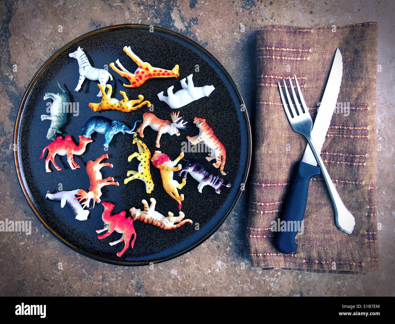 Kunststoff-Spielzeugtiere auf einem Teller neben Messer und Gabel. Stockfoto