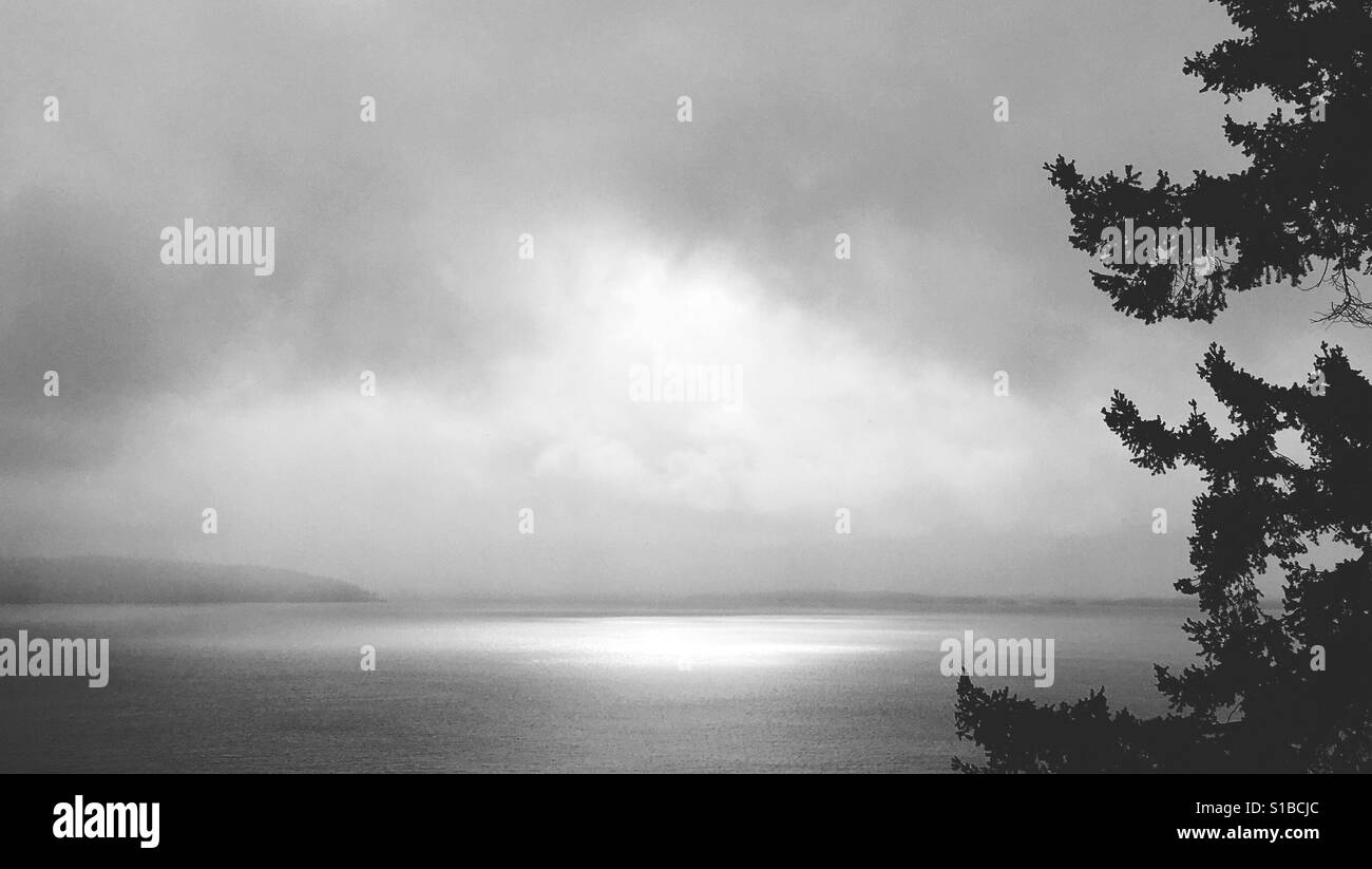 Dramatischen schwarz-weiß Foto der Sonne leuchtenden Punkt am Meer umgeben von dunklen Wolken. Stockfoto