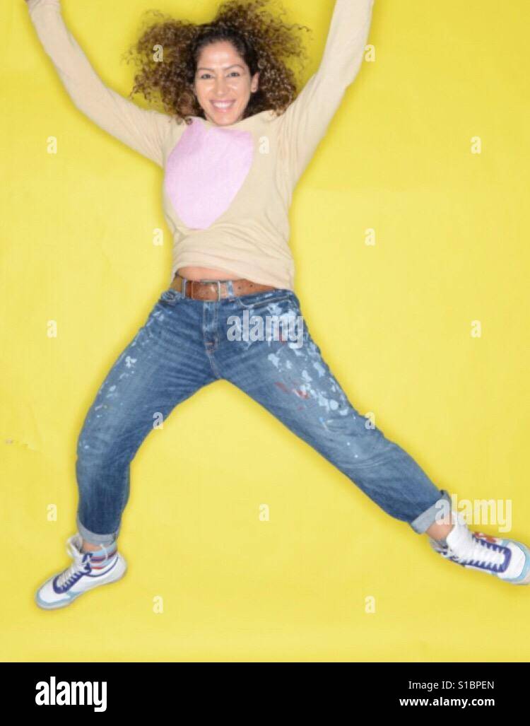 Frau mit bemalten Jeans und lockiges Haar mit einem gelben Hintergrund springen Stockfoto