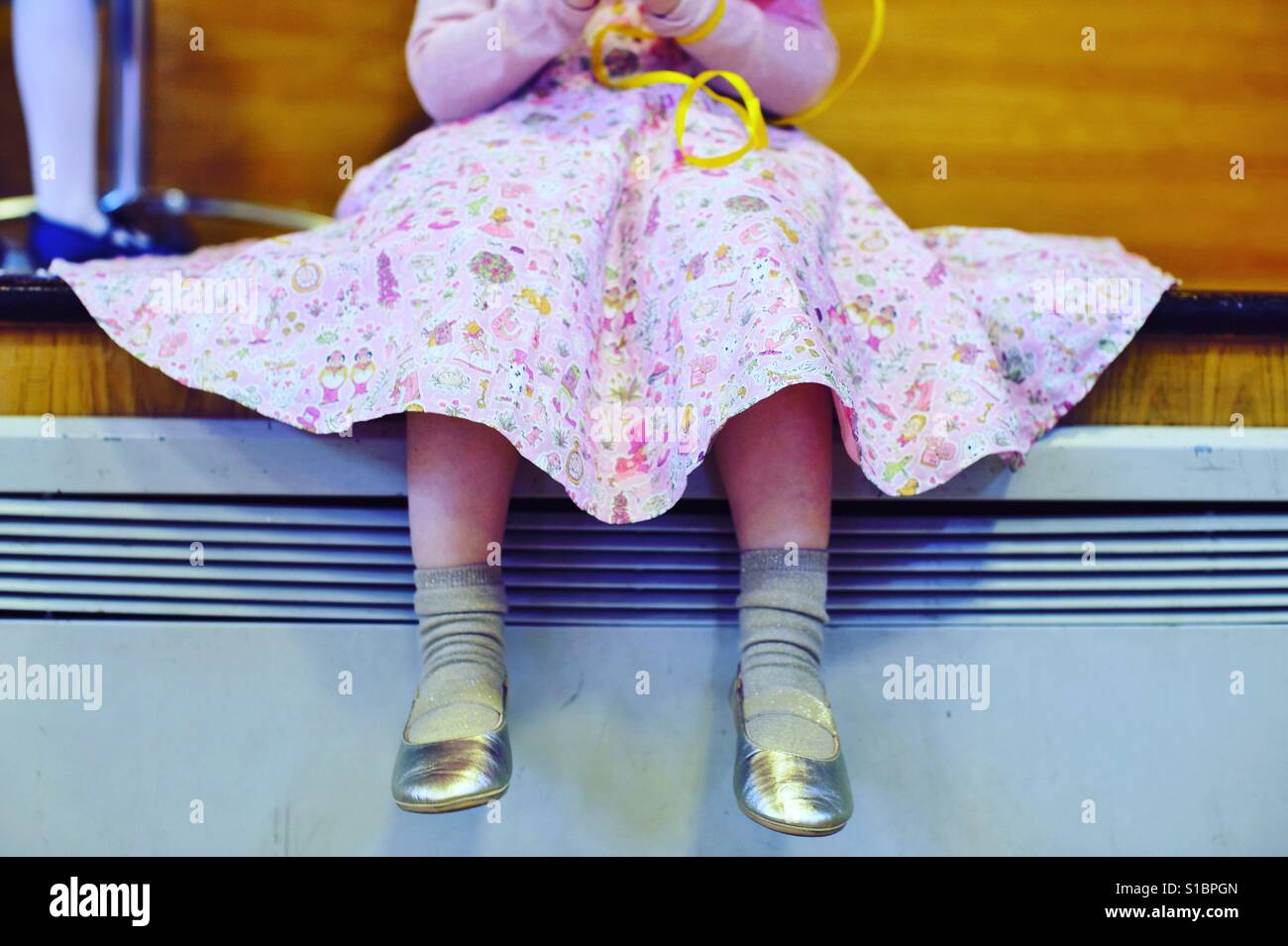 Kleines Mädchen sitzt mit guten Schuhen und rosa voller Rock Stockfoto