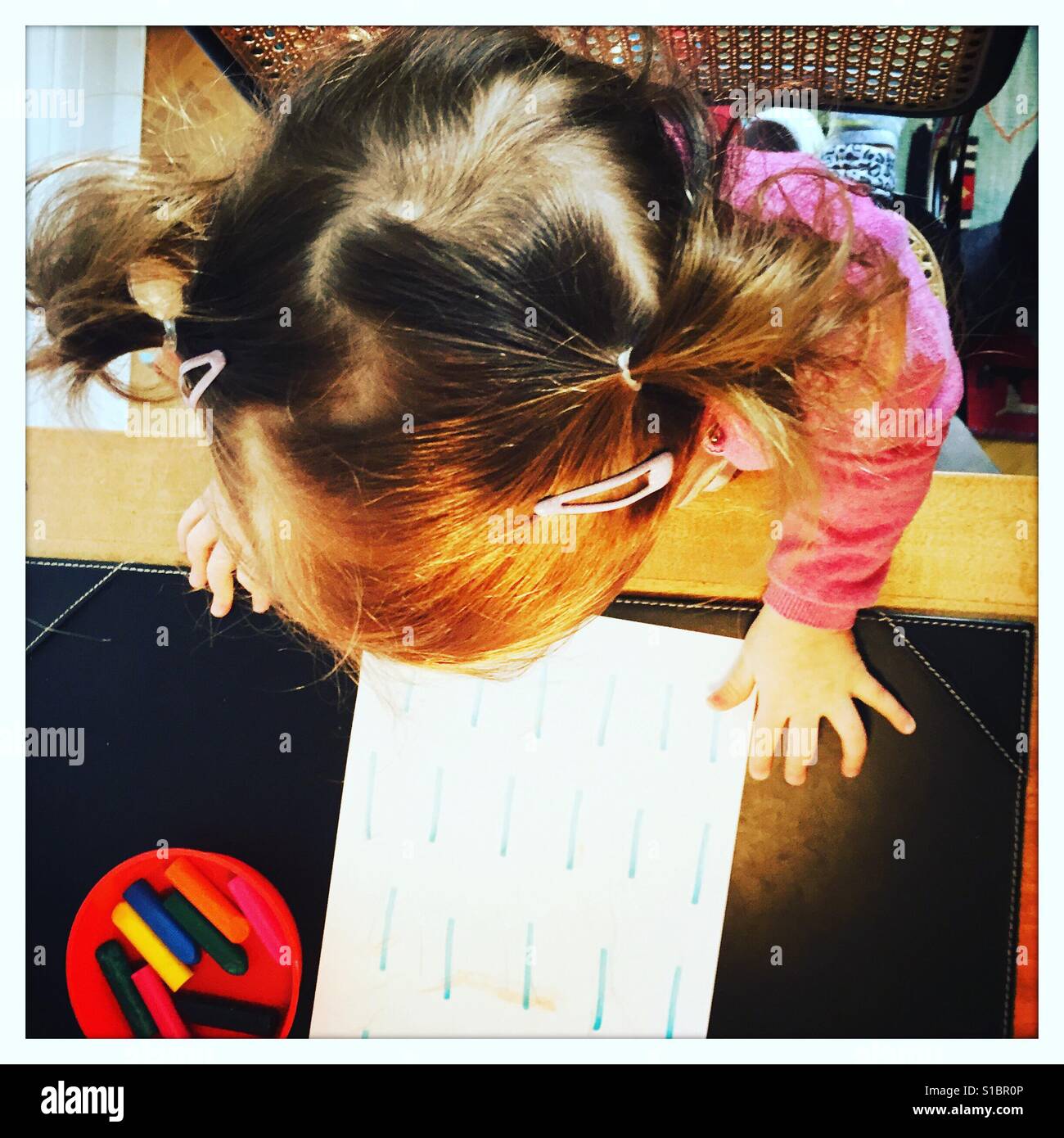 Kleinkind mit Zöpfen saß St Schreibtisch zeichnen mit Buntstiften Stockfoto