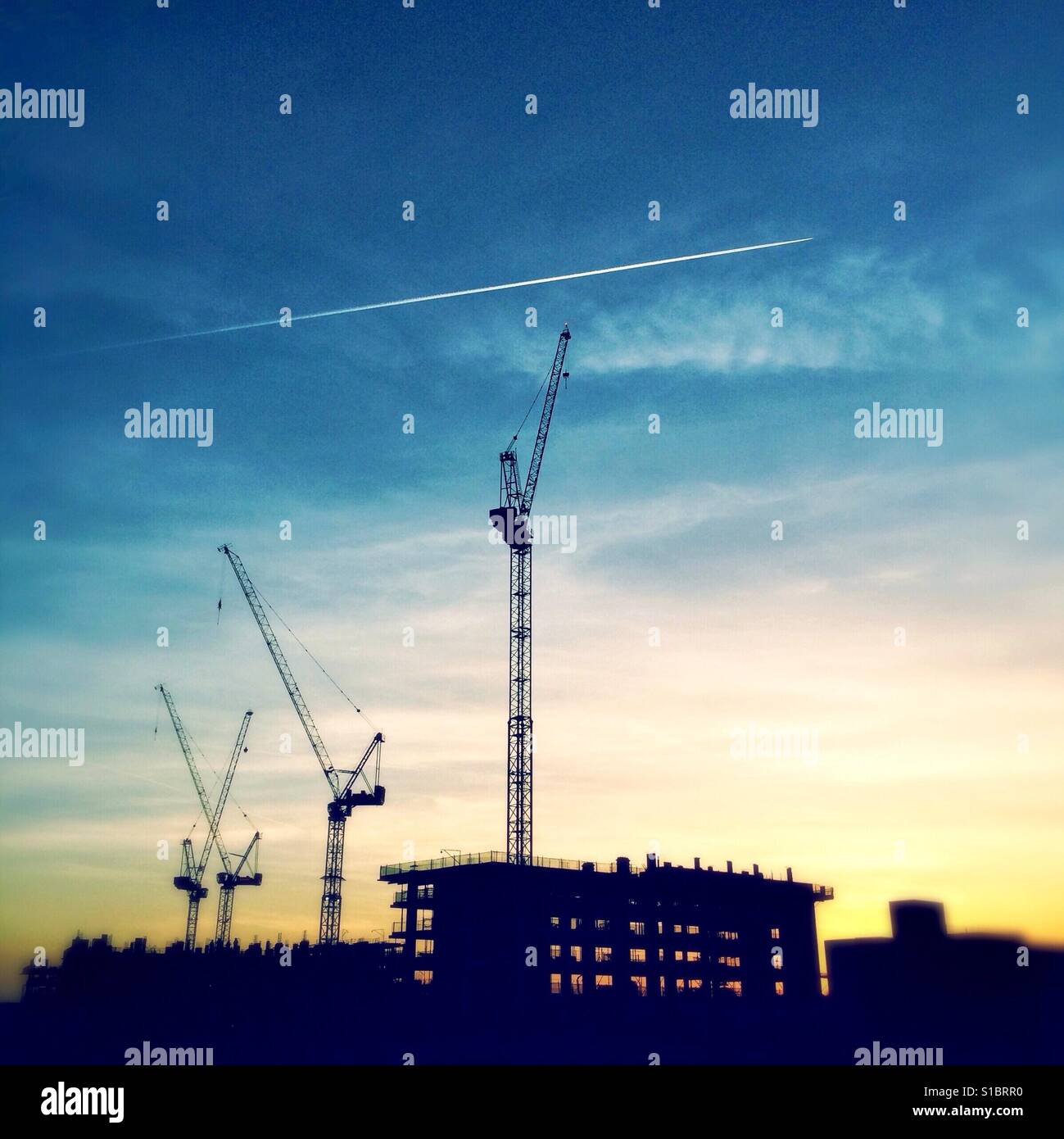 Krane, die Silhouette gegen den Abendhimmel, wie die Sonne über eine Baustelle in Colindale, Nordwesten Londons. Die Bauarbeiten ist Teil des Projekts Colindale Regeneration. Stockfoto