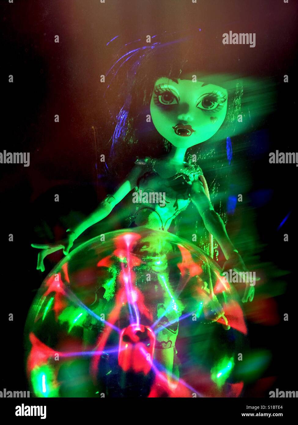 Eine Monster High Puppe mit gotischen Make-up steht hinter eine glühende Plasma-Kugel mit geisterhaften Effekt. Stockfoto