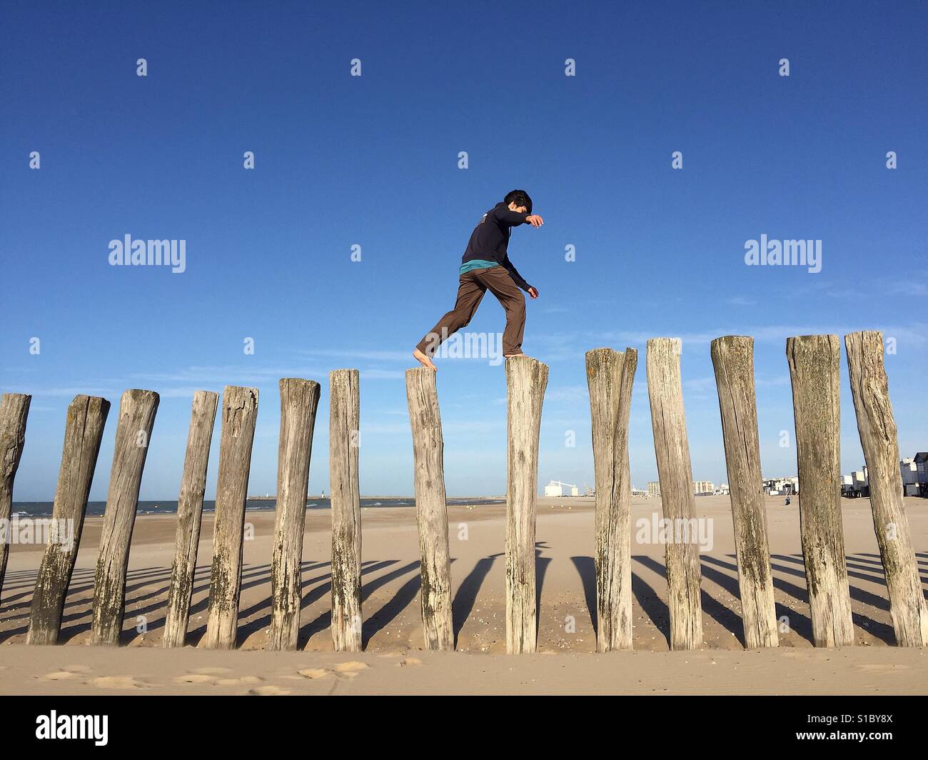 Mann springt auf hölzernen Säulen an einem sonnigen Strand in Calais Stockfoto