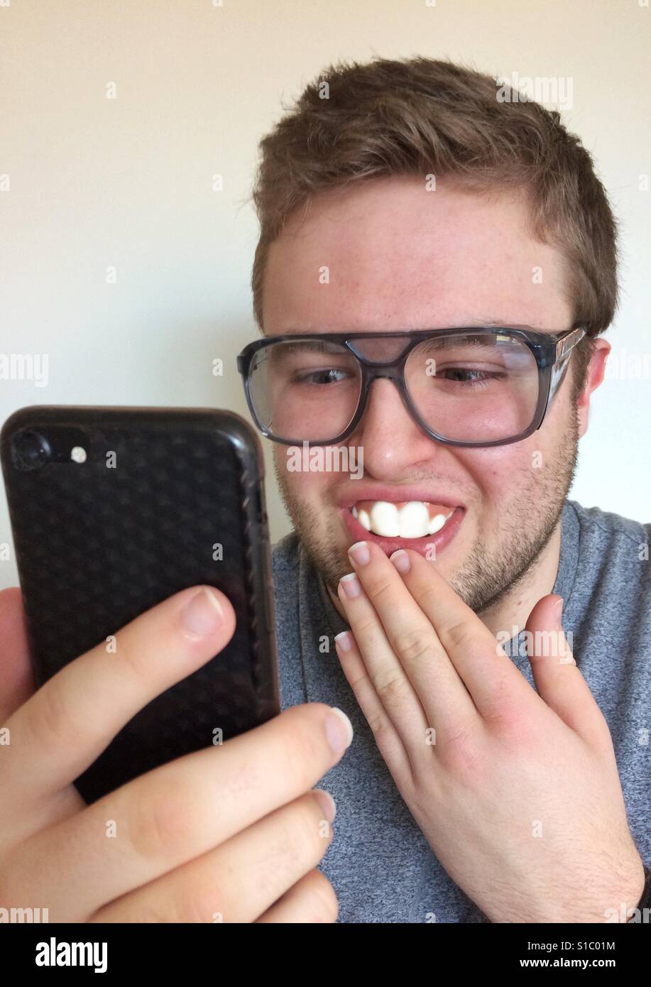Nerdy Teenager große Brille mit Buck Zähne, mit Blick auf sein Handy und sehr lachen. Stockfoto