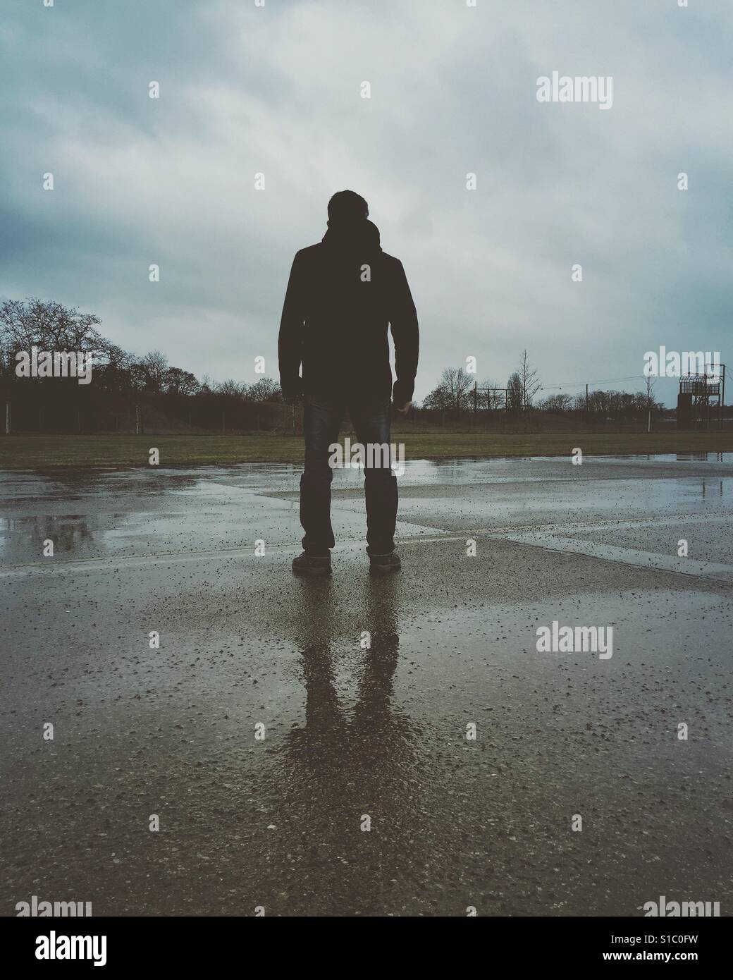 Rückansicht des eine finstere männliche Figur draußen im Regen stehen - Smartphone-aufgenommenes Stockfoto
