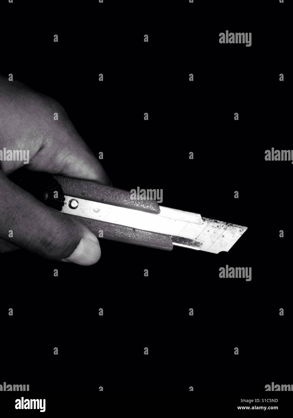 Hand Holding Cuttermesser - schwarz und weiß - schwarzen Hintergrund Stockfoto