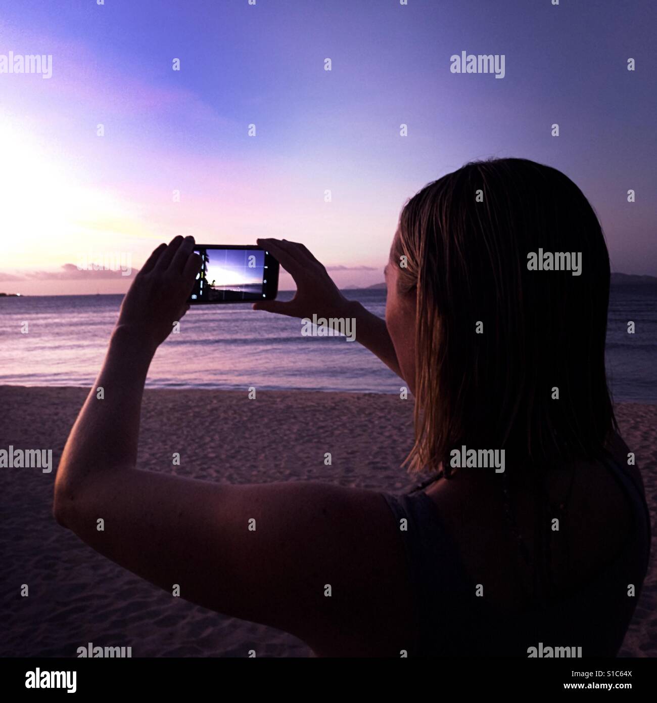 Eine junge Frau mache ein Foto des Sonnenuntergangs mit ihrem Smartphone. Tavarua Island, Fidschi. Stockfoto
