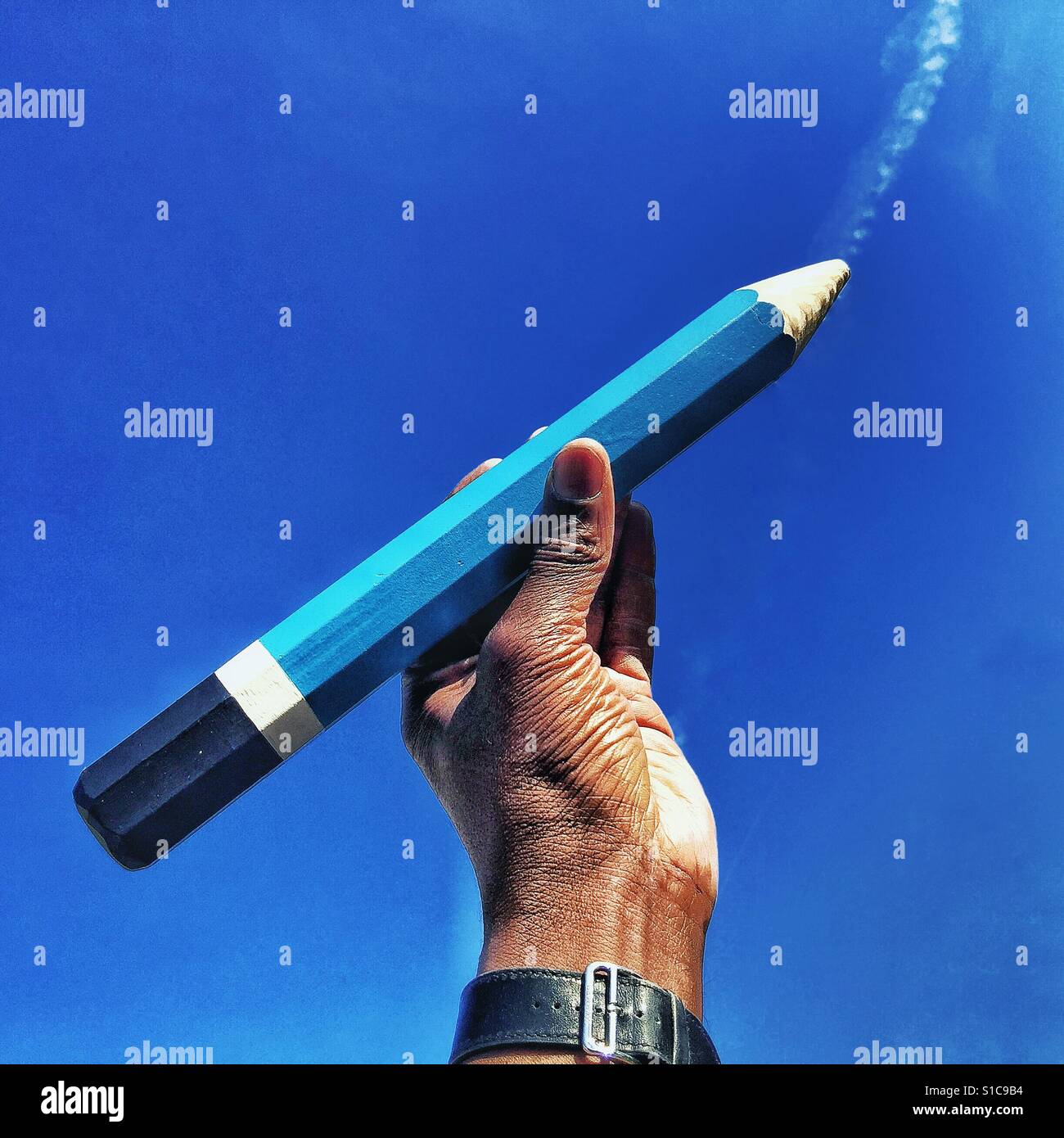 Hand, die einen riesigen Bleistift vor blauem Himmel. Stockfoto