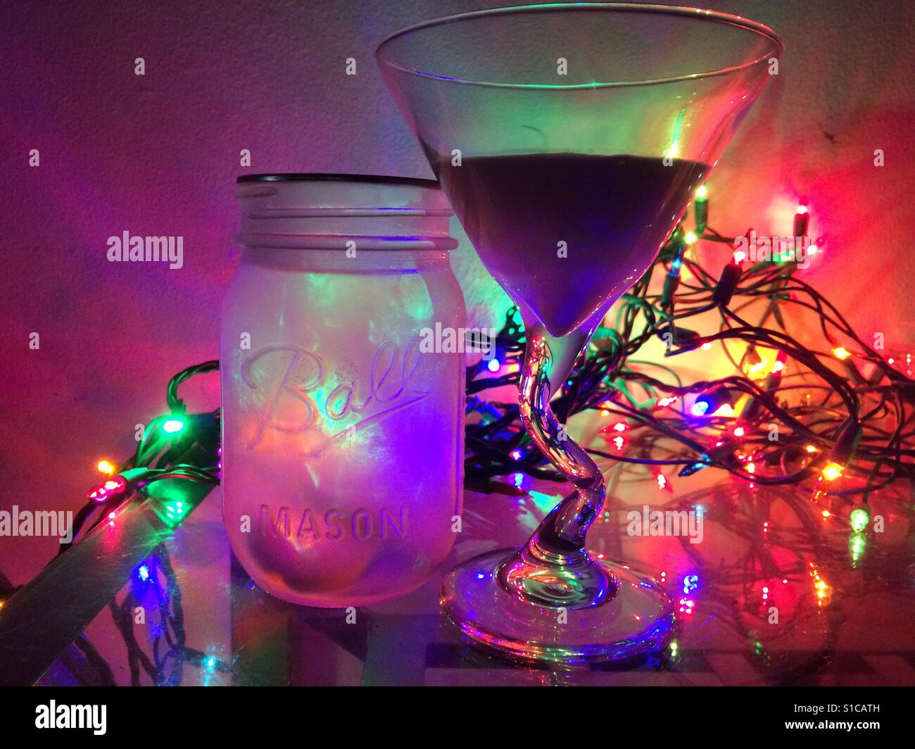 Bunte Lichter leuchten ein Einmachglas neben einem ausgefallenen Martini. Stockfoto