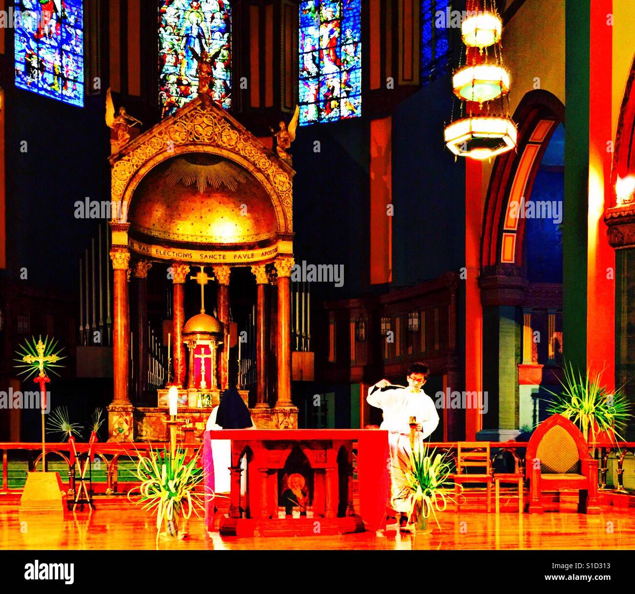 Junge Messdiener Schnupfen Kerze am Ende der Palmsonntag Masse umgeben von wunderschönen Kathedrale, Palm Prozessionskreuz, Palm Altar Dekorationen und zeremonielle Palmen wedeln. Stockfoto