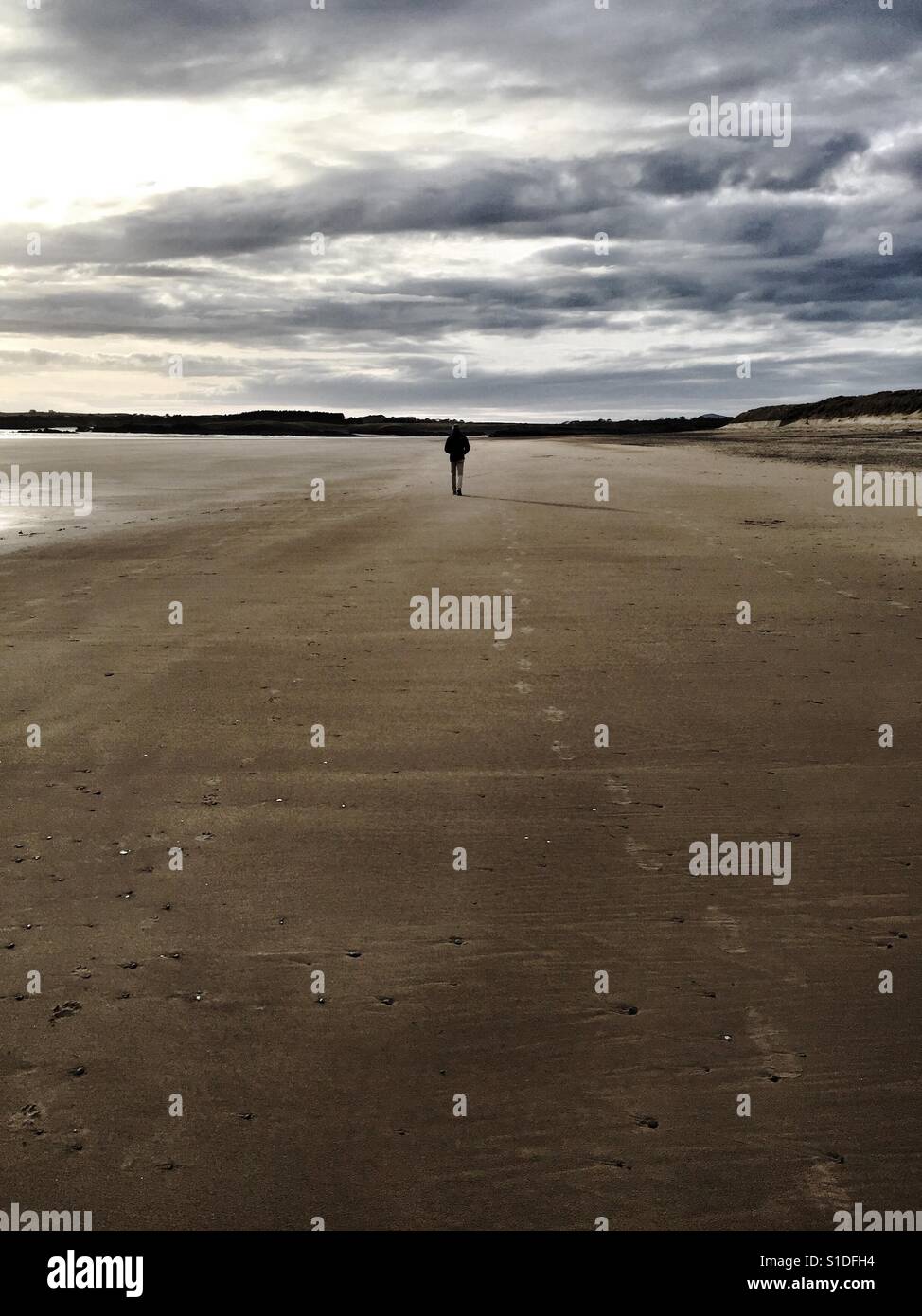 Mann zu Fuß tief in Gedanken versunken an einem Strand am Ende des Tages - Smartphone-aufgenommenes Stockfoto
