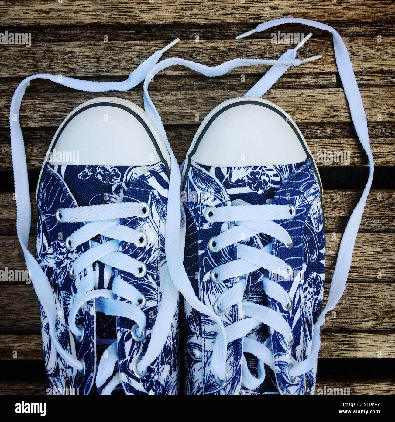 Leinwand-Converse-Stil-Trainer mit einer Surf-Stil blau-weiße Blume Muster drucken, gegen Holzterrassen fotografiert. Stockfoto