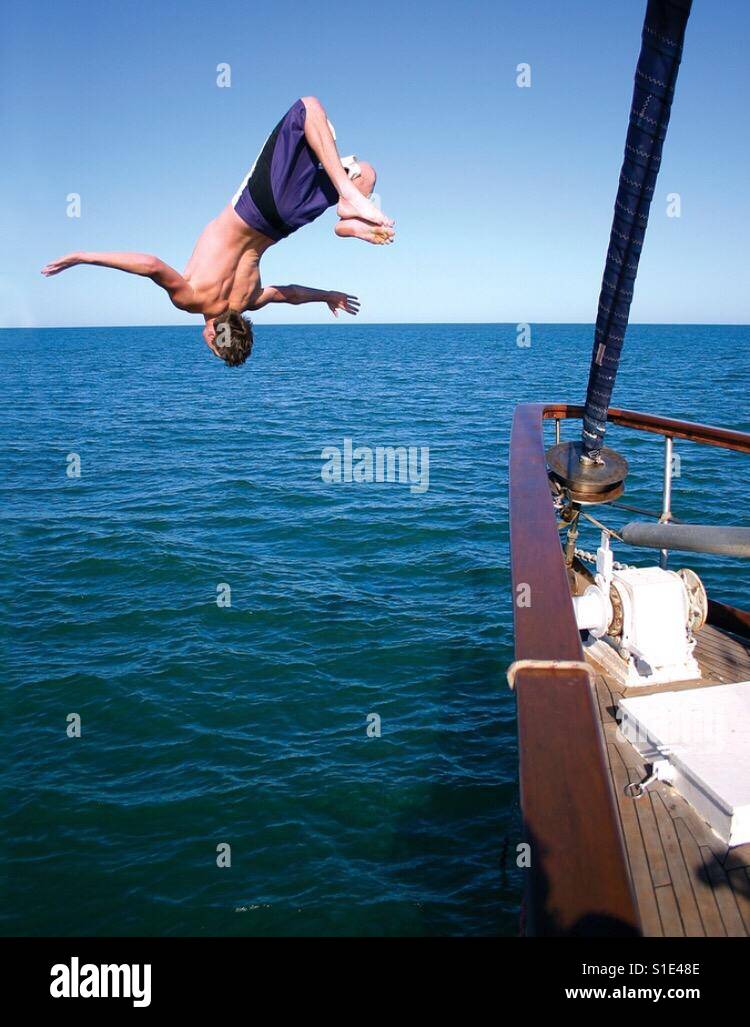 Ein junger Mann tut s Backflip aus den Bogen von einer Yacht ins Meer. Stockfoto