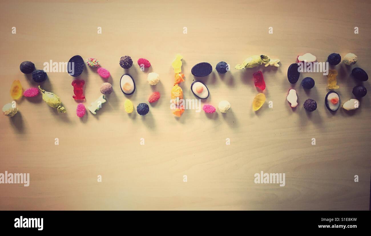 Das Wort "Addicted" mit Süßigkeiten und Bonbons auf einem Holztisch geschrieben Stockfoto