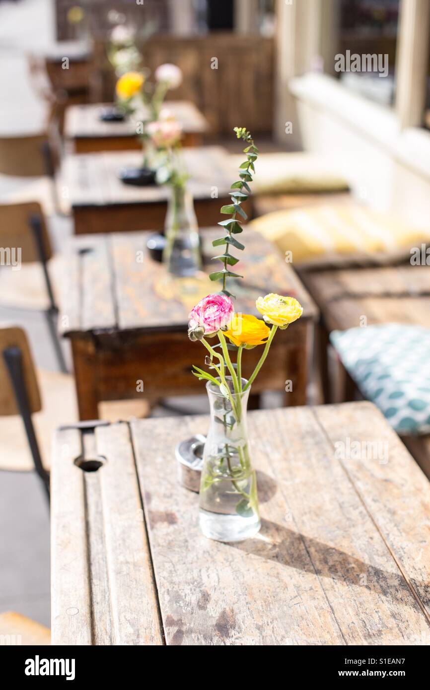 Hölzerne Tische draußen in der Sonne mit kleinen Blumenvasen alle in einer Reihe Stockfoto