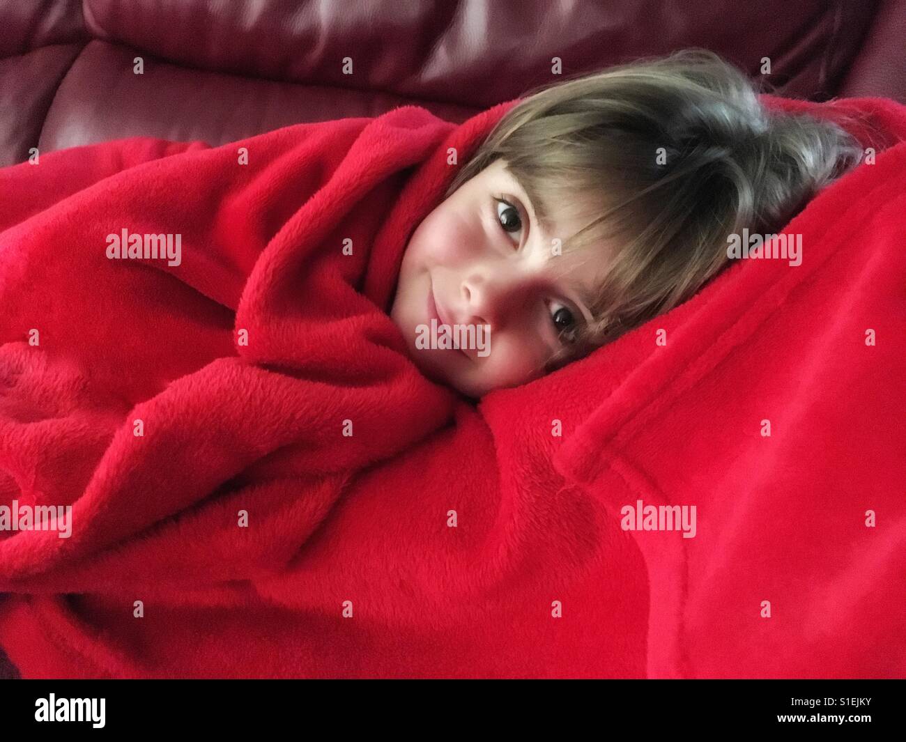 Niedliche kleine Mädchen Festlegung in einer weichen roten Decke eingewickelt. Lächelndes Gesicht der hübschen Kind krank zu Hause. Stockfoto