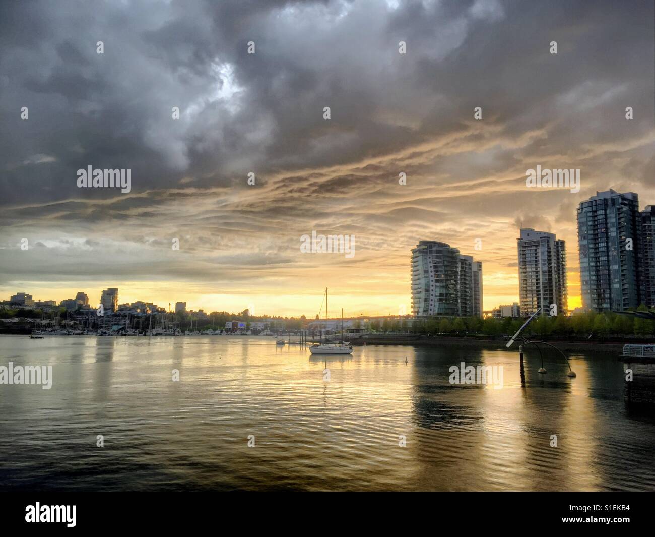 Sonnenuntergang in Vancouver am False Creek. Auf der rechten Seite Seite es drei hohe Steigleitung. Vor dem Wasser sind Wolken grau und gelb orange Stockfoto