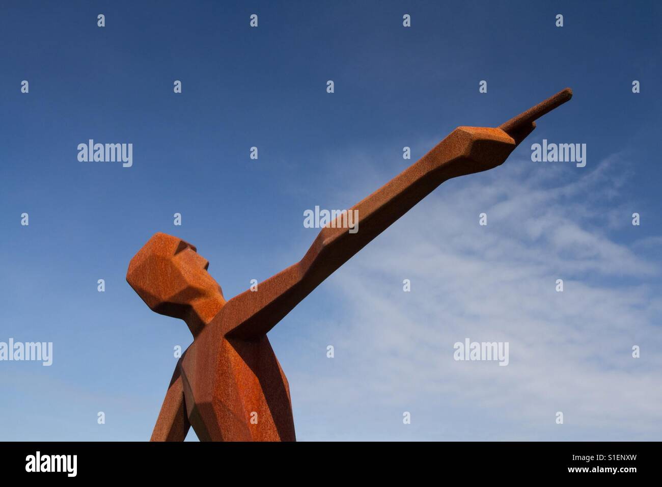 Eine Metall-Statue von einem schlanken Mann einen langen Arm ausstrecken und zeigte mit dem Finger direkt mit einem blauen Himmelshintergrund. - Smartphone-aufgenommenes Stockfoto