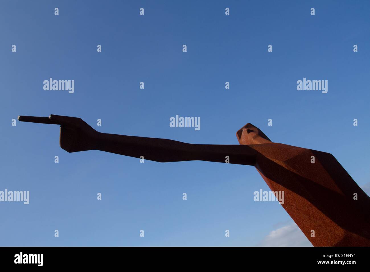 Eine hohe, schlanke Statue einer männlichen Figur mit ausgestrecktem Arm und zeigte mit dem Finger um den Weg mit einem blauen Himmelshintergrund zeigen. Stockfoto